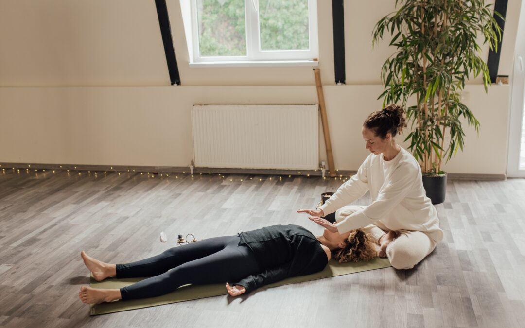 A person lying on a yoga mat in a white room with wooden floors and a plant having an energy healing alternative therapy