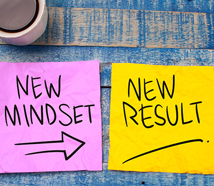Two small pieces of square paper next to each other to visually describe the stages of change. The left image on a pink piece of paper says new mindset with an arrow pointing to the yellow square paper next to it that has the words new results.